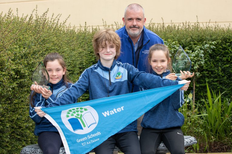 Three children holding a green schools blue water flag. Image - Bryan James Brophy