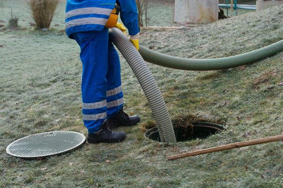 An engineers pumping out water from a drain hole using a tube.