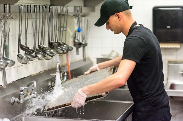 A kitchen porter washing a tray at the sink