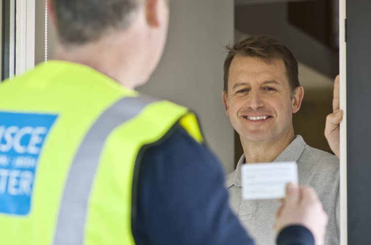 A man opening their house door to an Irish Water employee holding a card up.