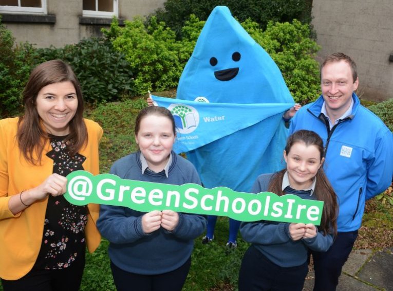 Two children and a teacher holding a green schools sign while the green schools 'droplet' mascot stands behind them