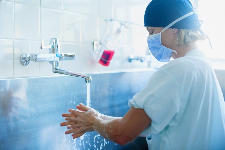 A surgeon washing their hands and arms as water pours the tap 