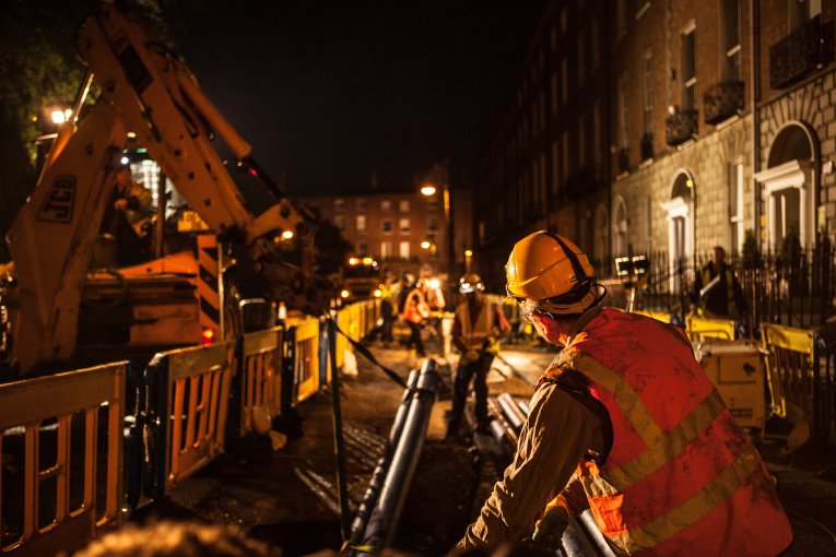 A worker assisting a crane in setting down a pipe during night time