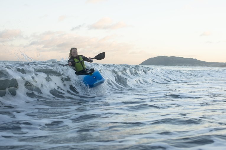 A woman within a kayak riding a wave
