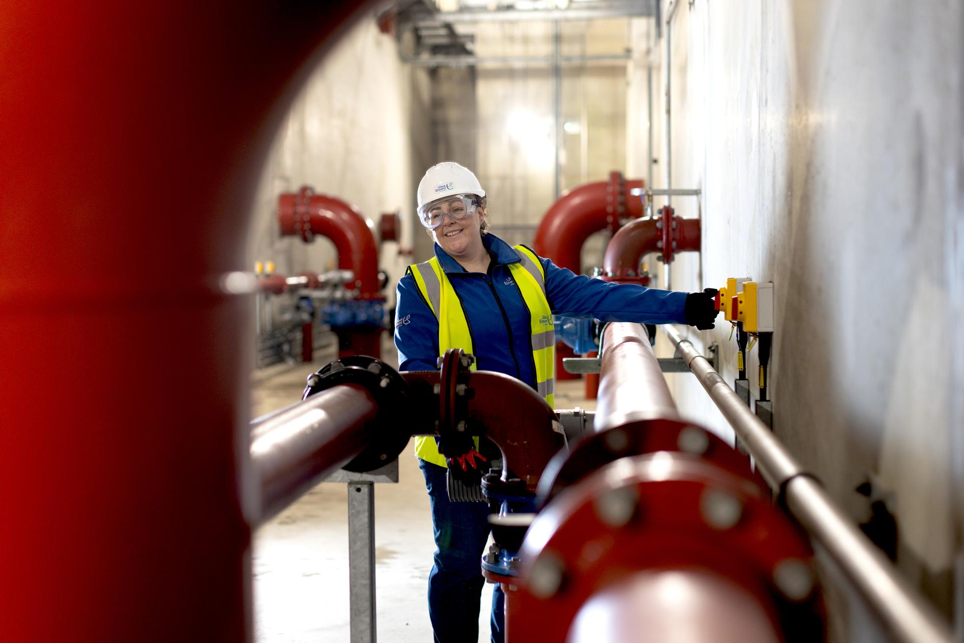 A person wearing safety gear pushing a red button on a wall surrounded by large red pipes