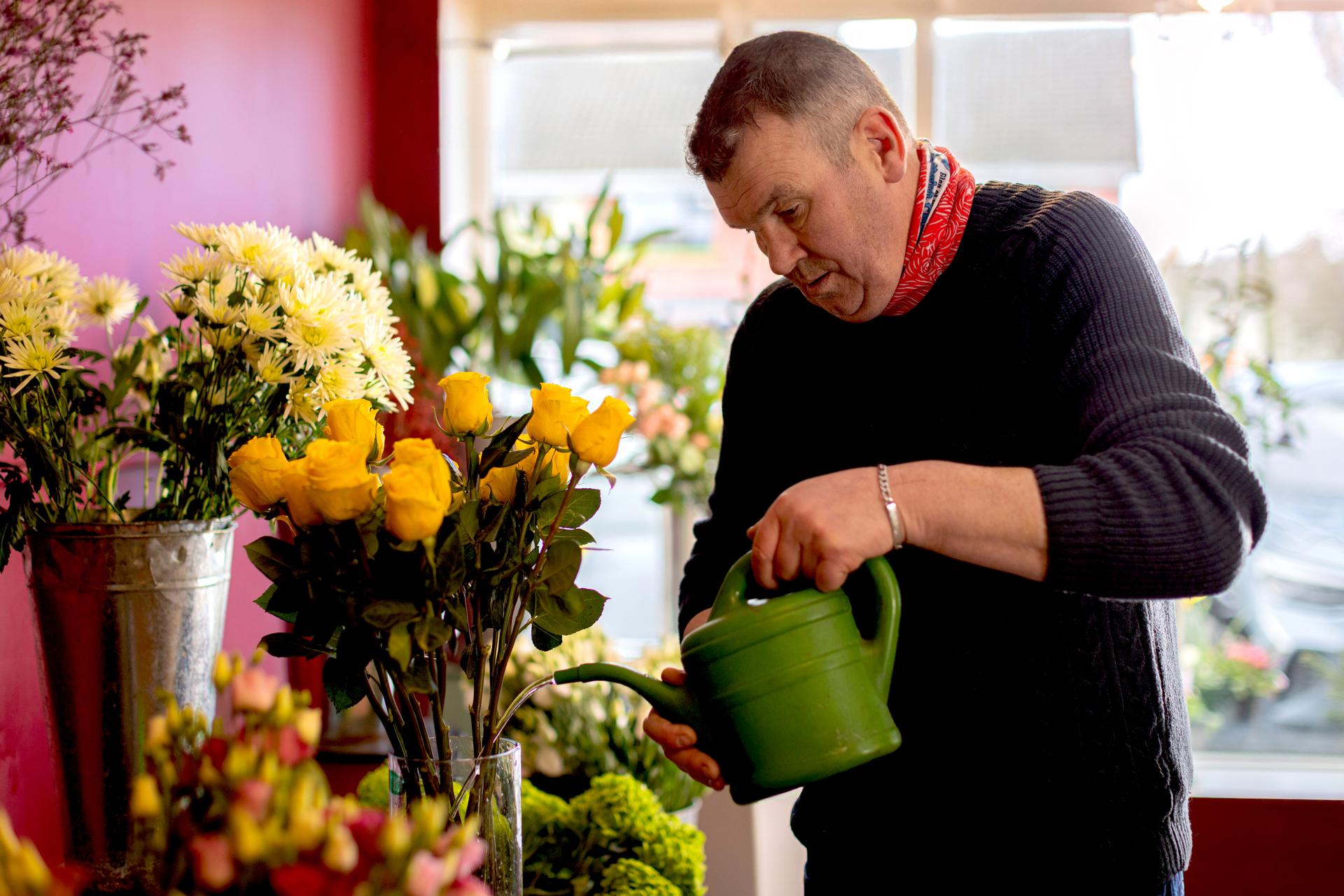 A florist watering a vase with flowers inside a shop