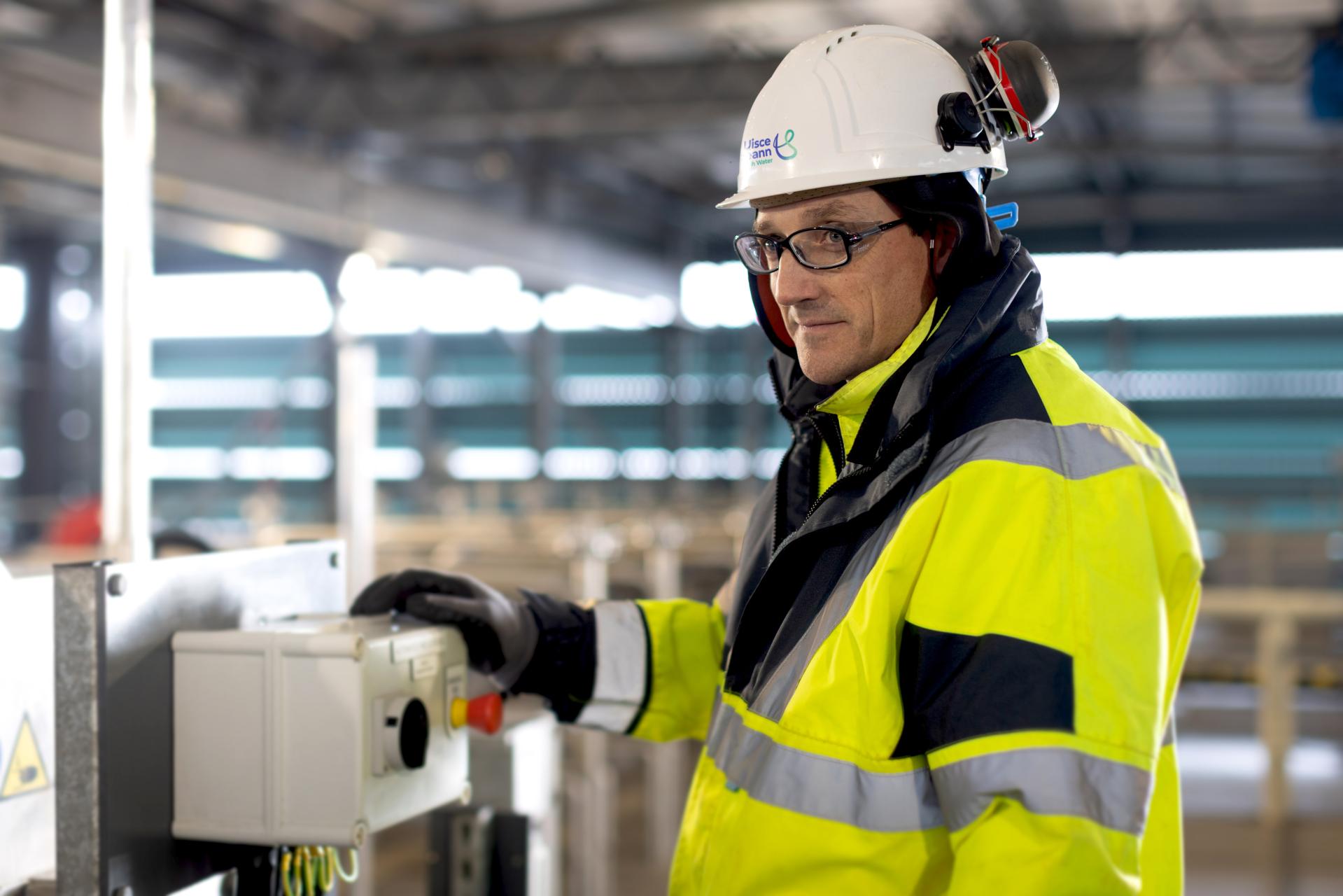 A UÉ worker standing by a red start / stop button in a industrial unit