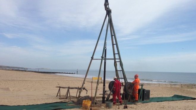 Two people digging a borehole on a beach