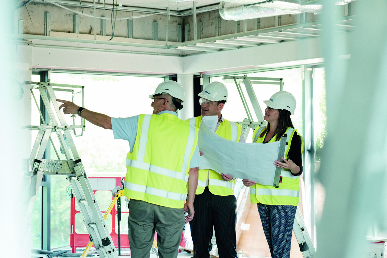 Three engineers looking at plans inside a building wearing safety gear 