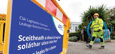 Uisce Éireann carrying a rolled up plastic blue pipe walking across an Uisce Éireann signage about fixing leaks