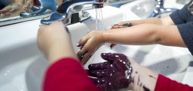 Kids with paint on their hands washing their hands in a sink