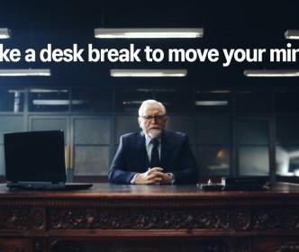 A person sitting on a office desk looking to the camera with "Take a desk break to move your mind" caption above him