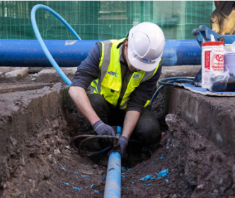 An Uisce Éireann worker fixing a blue pipe in the ground