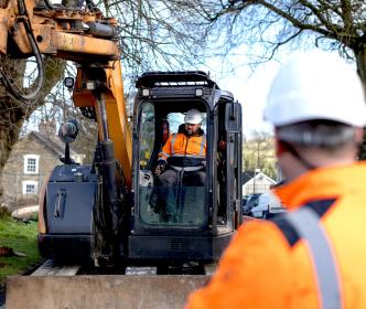 An engineer using a digger and another engineer inspecting the work