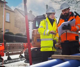 Two Uisce Éireann engineers doing road works with pipes looking at plans
