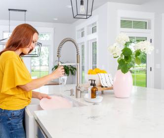A person wearing a yellow shirt washing dishes using a hose on a tap in a white coloured kitchen