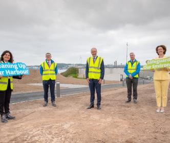 Micheal Martin standing with UÉ board members at a construction site holding signs for cleaning up the harbour and the environment
