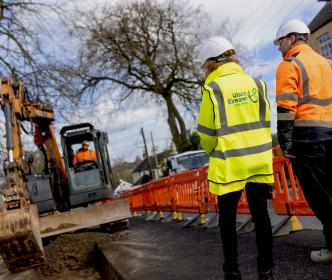 Two engineers during a road work while another engineer is using a digger