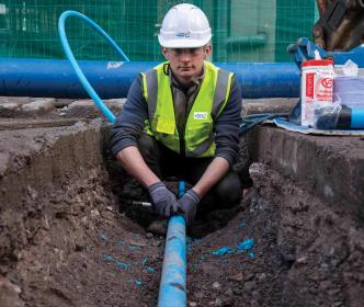 An Uisce Éireann worker fixing a blue pipe in the ground