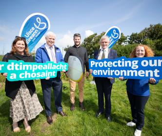 Three people holding shovels, and one man holding a surfboard with a sign reading "Safeguarding our environmant"