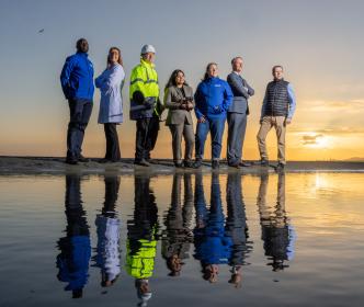 A group of Uisce Éireann workers by the sea with a sunset