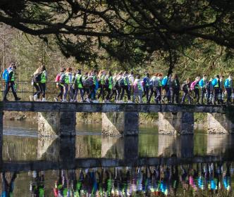 A group of children wearing hi-vis jackets walking across a bridge over a river