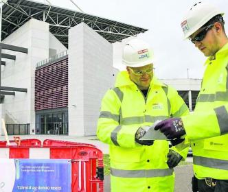 Two Uisce Éireann workers looking at plans on a site by a large buildings